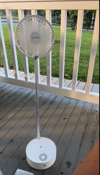 A white fan on an extended pole on a porch 
