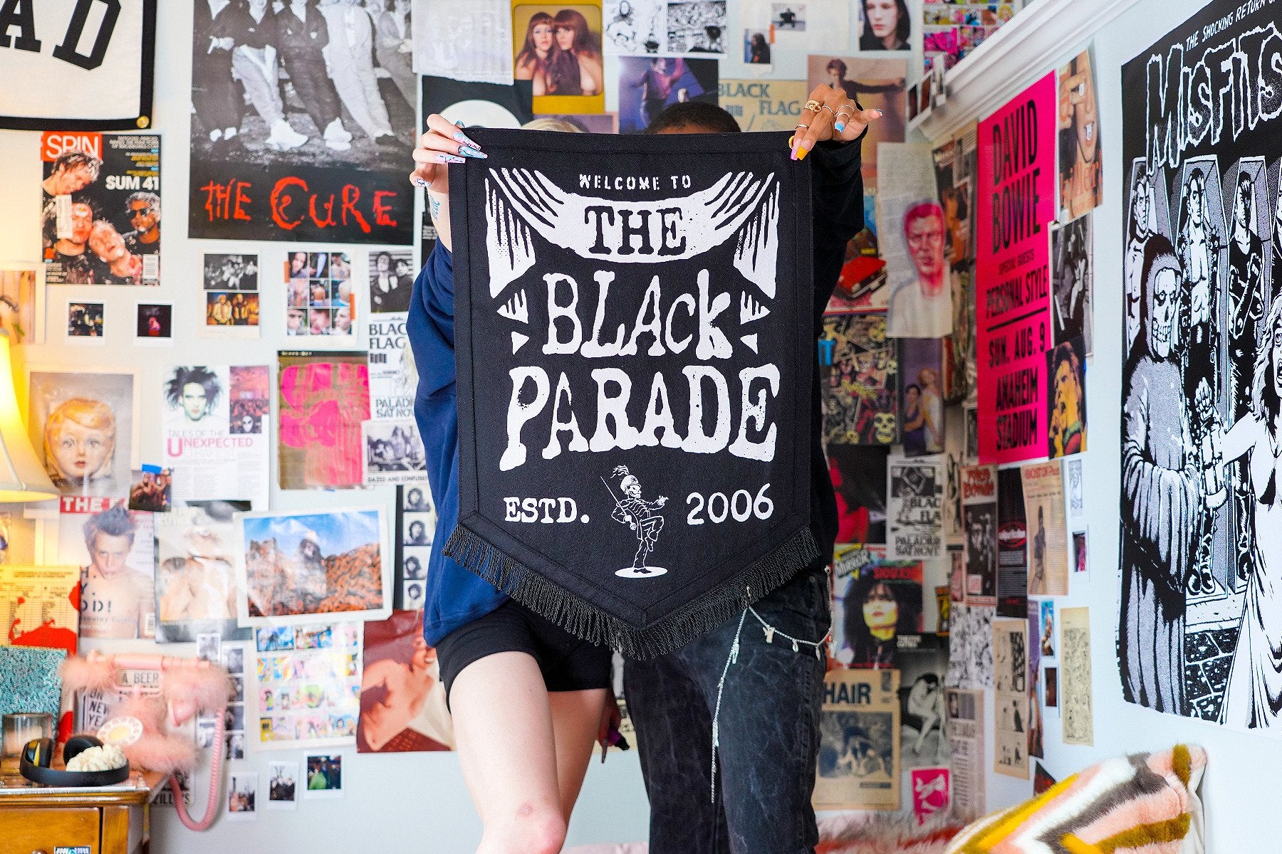 Two people holding up the banner in front of a magazine-covered bedroom wall