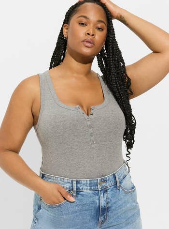Model in a gray button-front casual tank top and jeans, hand on head