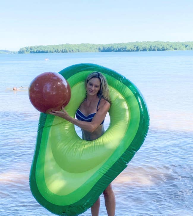 Reviewer holding avocado pool float with hole and a brown ball that's meant to be the pit 