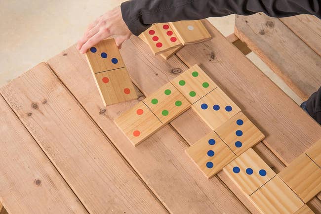 A person arranges large wooden domino tiles with colored dots on a wooden table