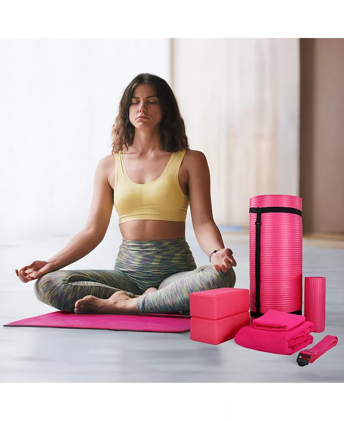 Woman in workout attire meditates on a mat surrounded by yoga gear, including blocks and a roller