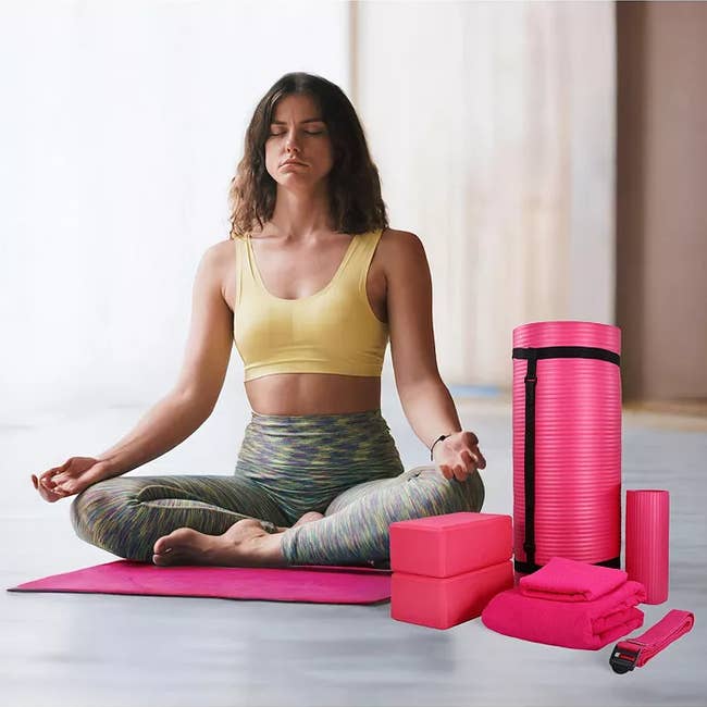 Woman in workout attire meditates on a mat surrounded by yoga gear, including blocks and a roller