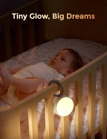Baby lying successful  crib with soft-glow nightlight attached to rail, creating a warm, dreamy ambiance. Text reads, 