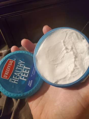 Hand holding an unfastened instrumentality of O'Keeffe's Healthy Feet Foot Cream, showing the pick inside