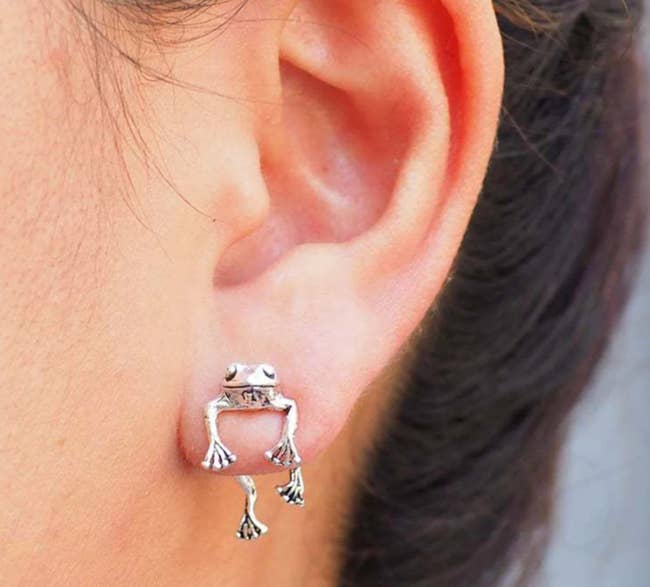 Model is wearing a tiny frog stud earring that looks like its hanging from your lobe through the piercing hole