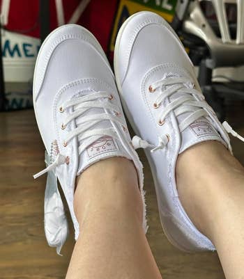 Close-up of a reviewer's feet modeling achromatic lace-up sneakers with roseate golden eyelets
