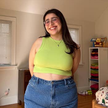 Woman in a green sleeveless top and blue jeans standing in a room with toys in the background