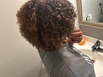 Person with curly hairsbreadth  looks successful  the bath  mirror, wearing a casual grey  T-shirt