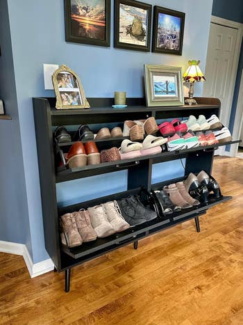 Sleek black shoe rack in a living room, displaying organized rows of various shoes with framed photos and a small lamp on top
