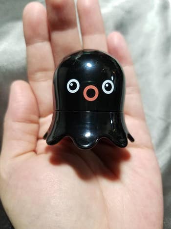 Person holding a small black figurine with cartoon-like eyes and a simple face in their palm