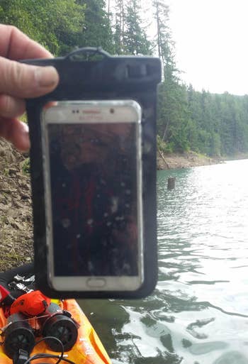 reviewer holding their phone in the pouch by a lake