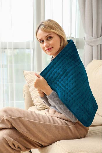Model wearing large blue rectangular heating pad draped over their shoulders