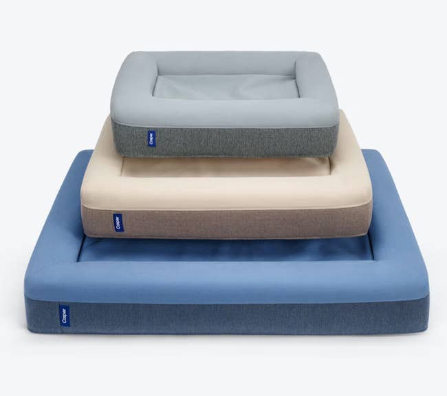 Blue, brown, and gray different sized dog beds stacked on top of one another on white background