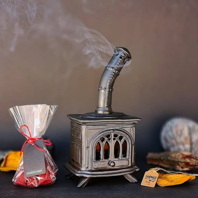 A tiny decorative metallic stove with smoke, adjacent to a wrapped container of cones