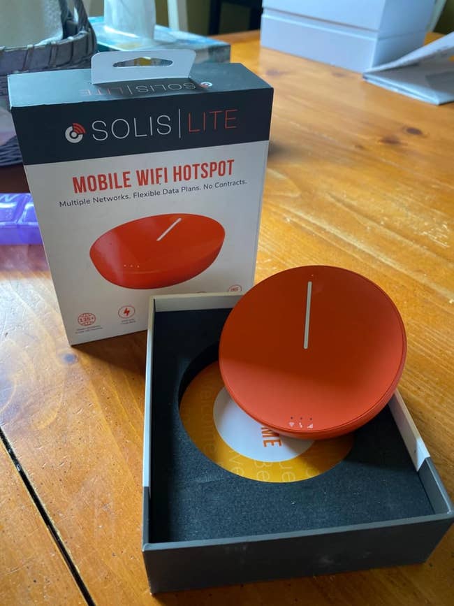 Solis Lite mobile WiFi hotspot in its packaging, featuring a round orange device and the box that highlights multiple networks and flexible data plans