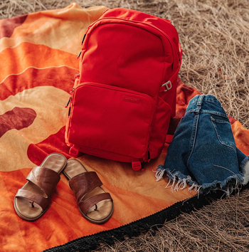 the red backpack on a blanket next to a pair of sandals and shorts