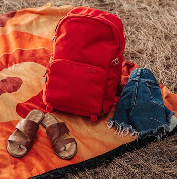 the red backpack on a blanket next to a pair of sandals and shorts