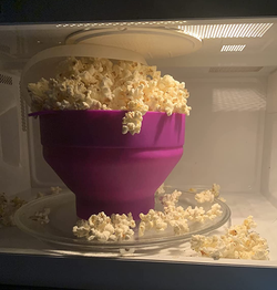 popcorn maker inside of a microwave, with fresh popcorn overflowing from the lid