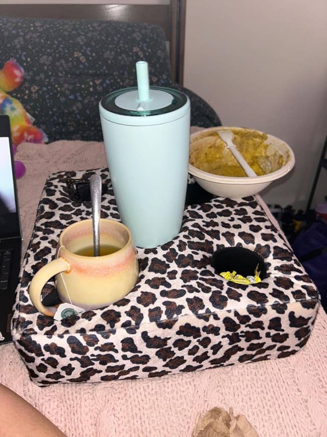 Lap tray with leopard print design holding a drink, a mug with a spoon, and a bowl of soup, set on a couch