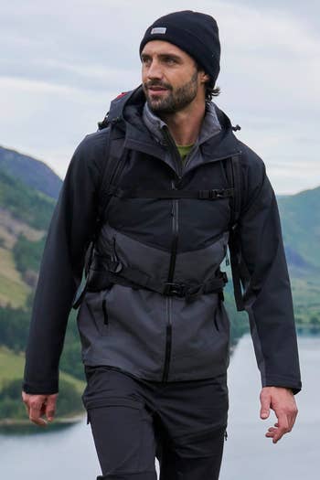 Person wearing outdoor hiking gear walking near a scenic lake and mountains, promoting stylish and functional adventure clothing