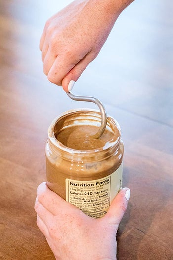 A model using a metal squiggly shaped stirrer to mix a jar of natural peanut butter  