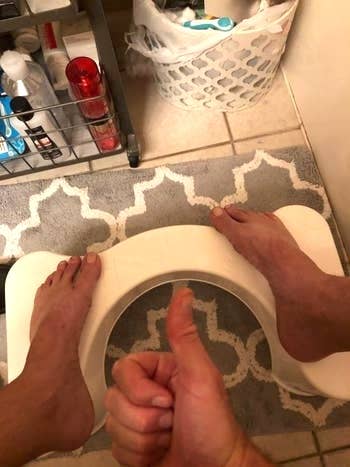 a reviewer with their feet on the stool holding a thumbs up