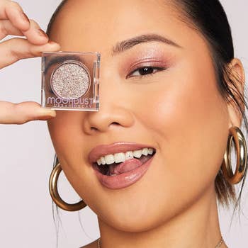 a model wearing pink sparkly eyeshadow and holding the packaged product up to their eye