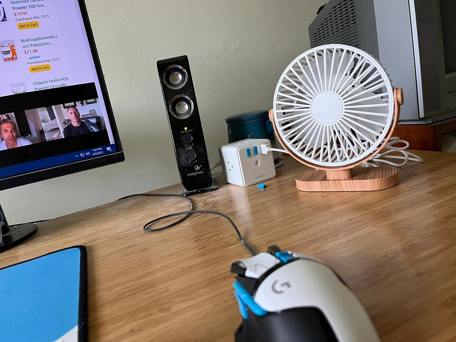 Small white and wood table fan on a wooden desk, next to a surge protector and a computer mouse