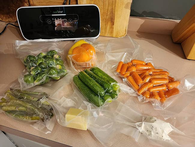 a reviewer photo of the vacuum sealer surrounded by different foods in vacuum sealed bags 