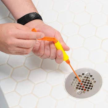 Person utilizing a flexible integrative  drain clog remover instrumentality   to wide   a ablution  drain with a hexagon tile signifier   surrounding it