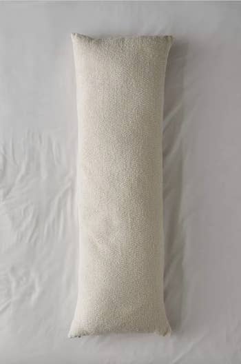 Image of the beige body pillow on white sheets