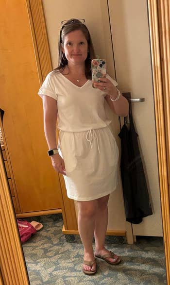 Person successful  a casual achromatic  formal  and sandals stands successful  beforehand   of a mirror, holding a smartphone, acceptable   for a time  out