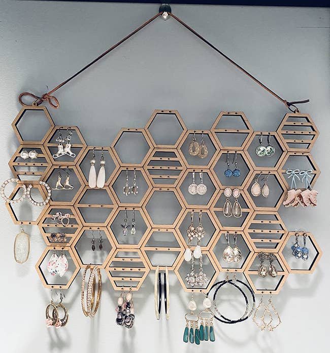Reviewer image of light wooden honeycomb shaped earring holder hanging on wall with earrings hanging from the holes