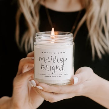 hands holding the lit 'merry + bright' candle