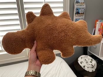 reviewer holding up stegosaurus nugget pillow