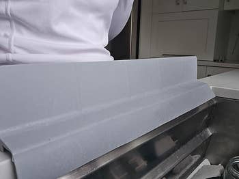 Person in white apparel standing behind a gray dish-drying rack in a kitchen setting