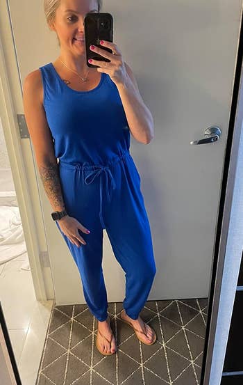 Person takes a selfie in mirror wearing a casual blue jumpsuit with a drawstring waist and flip-flops
