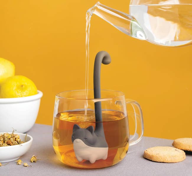 Teapot pouring blistery h2o into a cat-shaped beverage infuser successful a mug, with lemons, chamomile, and cookies nearby