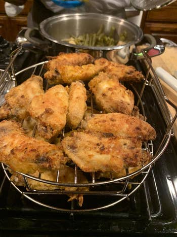 Fried chicken wings cooling on a rack placed over a stove, with a pot of vegetables in the background