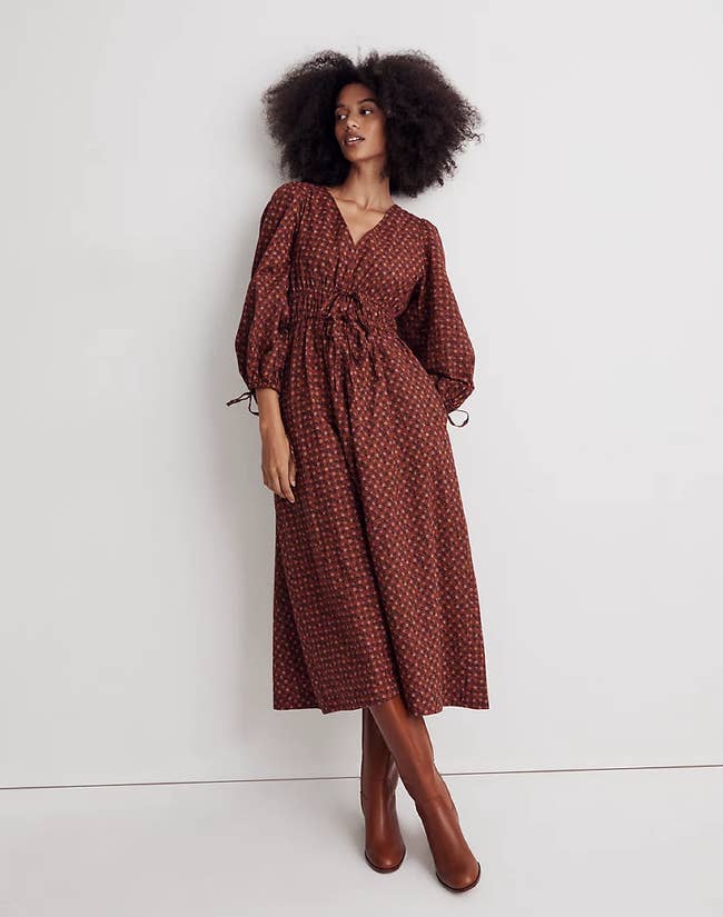 Model wearing red puff sleeved midi dress with floral pattern and tie waist paired with brown boots on a white background