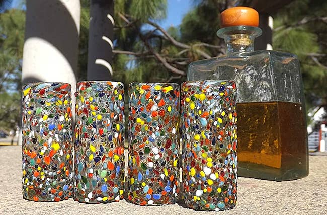 four colorful confetti shot glasses in front of a bottle of brown liquor