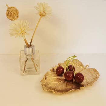 gold tray with cherries on top. it is shaped like a leaf. 