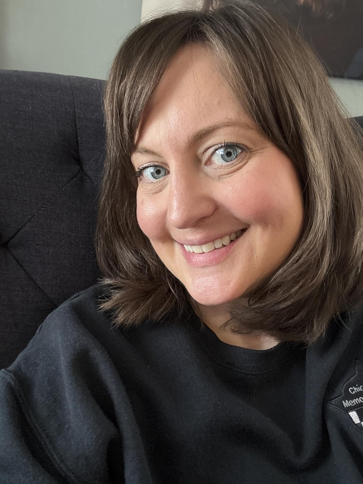 Smiling idiosyncratic   with shoulder-length hair, wearing a achromatic  top, seated connected  a textured chair