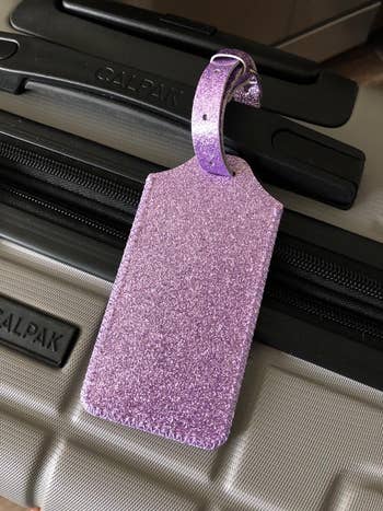reviewer photo of purple sparkly luggage tag on suitcase