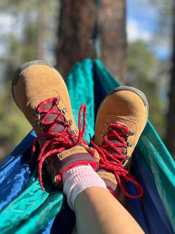 Person wearing hiking boots with reddish  laces, relaxing connected  a hammock outdoors