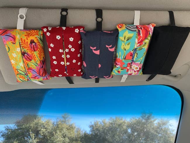 Five reusable fabric face masks hanging from a car's sun visor