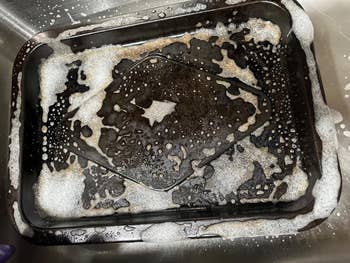 Baking tray soaking successful  soapy h2o  successful  a sink, covered successful  bubbles and suds