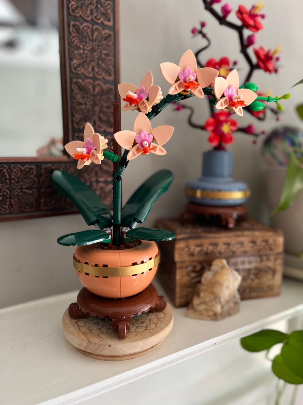Lego orchid exemplary  connected  a shelf, with greenish  leaves, pinkish  flowers, orangish  pot, and brownish  stand