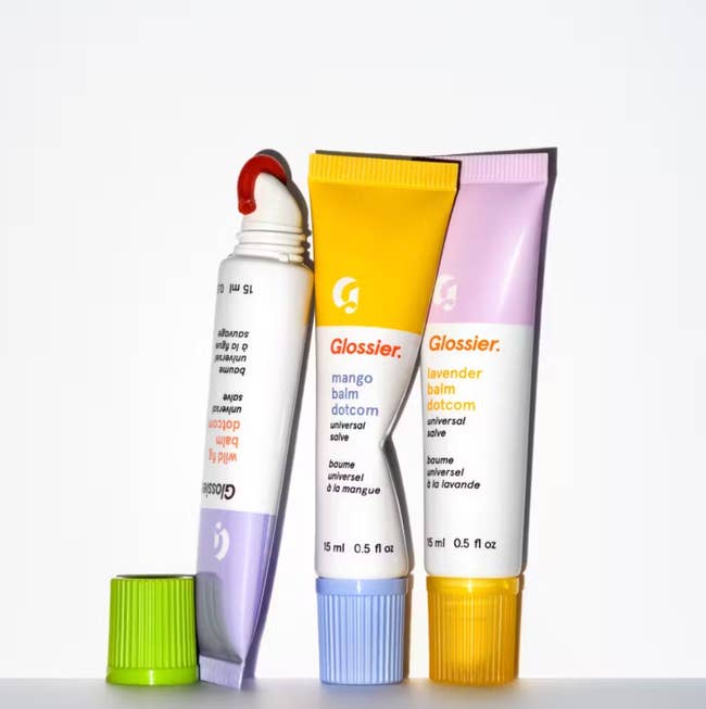 Three Glossier lip balm tubes in varying flavors are standing against a white background